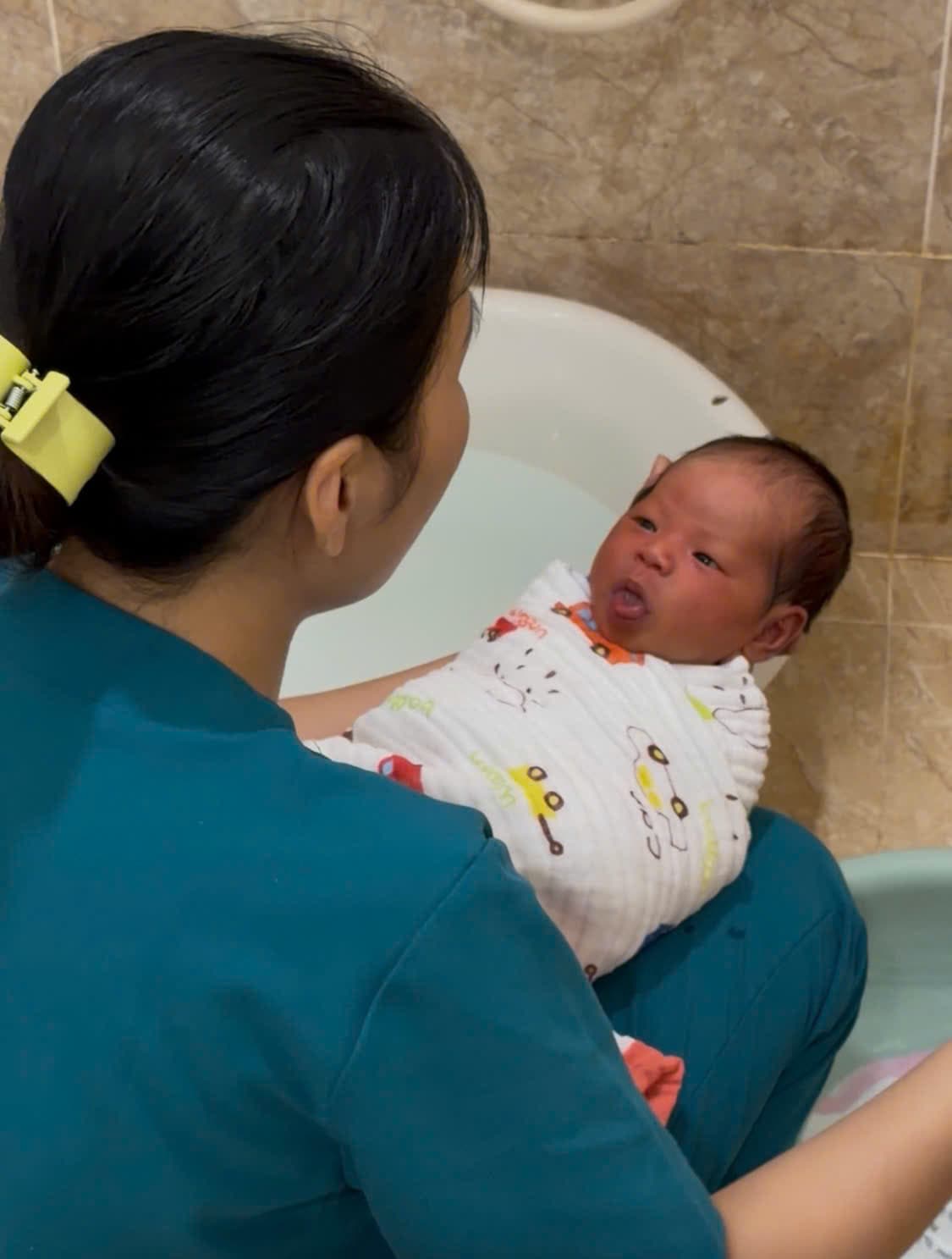 Chuyên viên Be Care đỡ bé trong chậu tắm, kiểm soát nhiệt độ nước