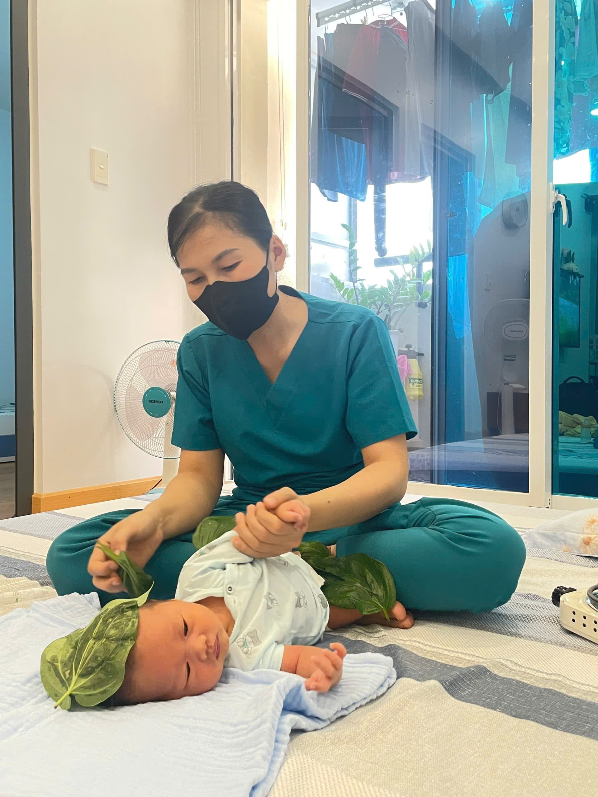 Chuyên viên Be Care đắp lá trầu trên đầu và bụng bé sơ sinh